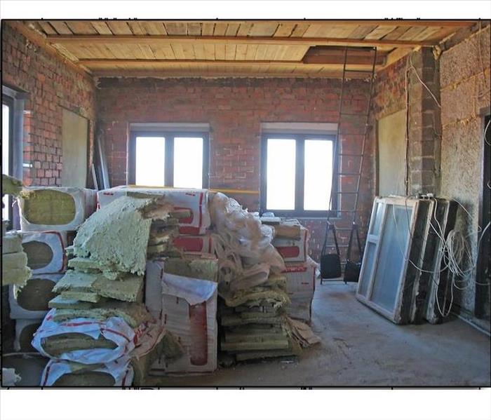 A room in and industrial buidling with bare brick walls, exposed wood planks on the ceiling, and stacks of bat insulation;