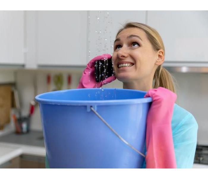 A woman holding a bucket catching water on a phone. 