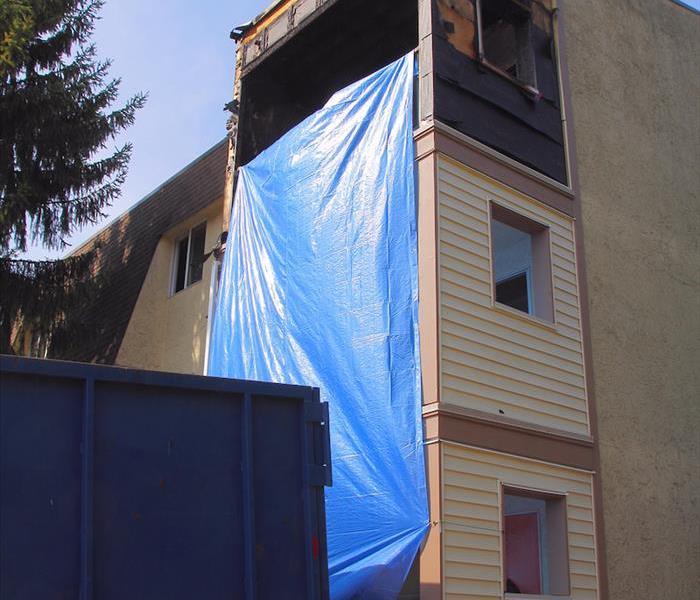 A fire in a commercial business with a blue tarp up and a dumpster. 